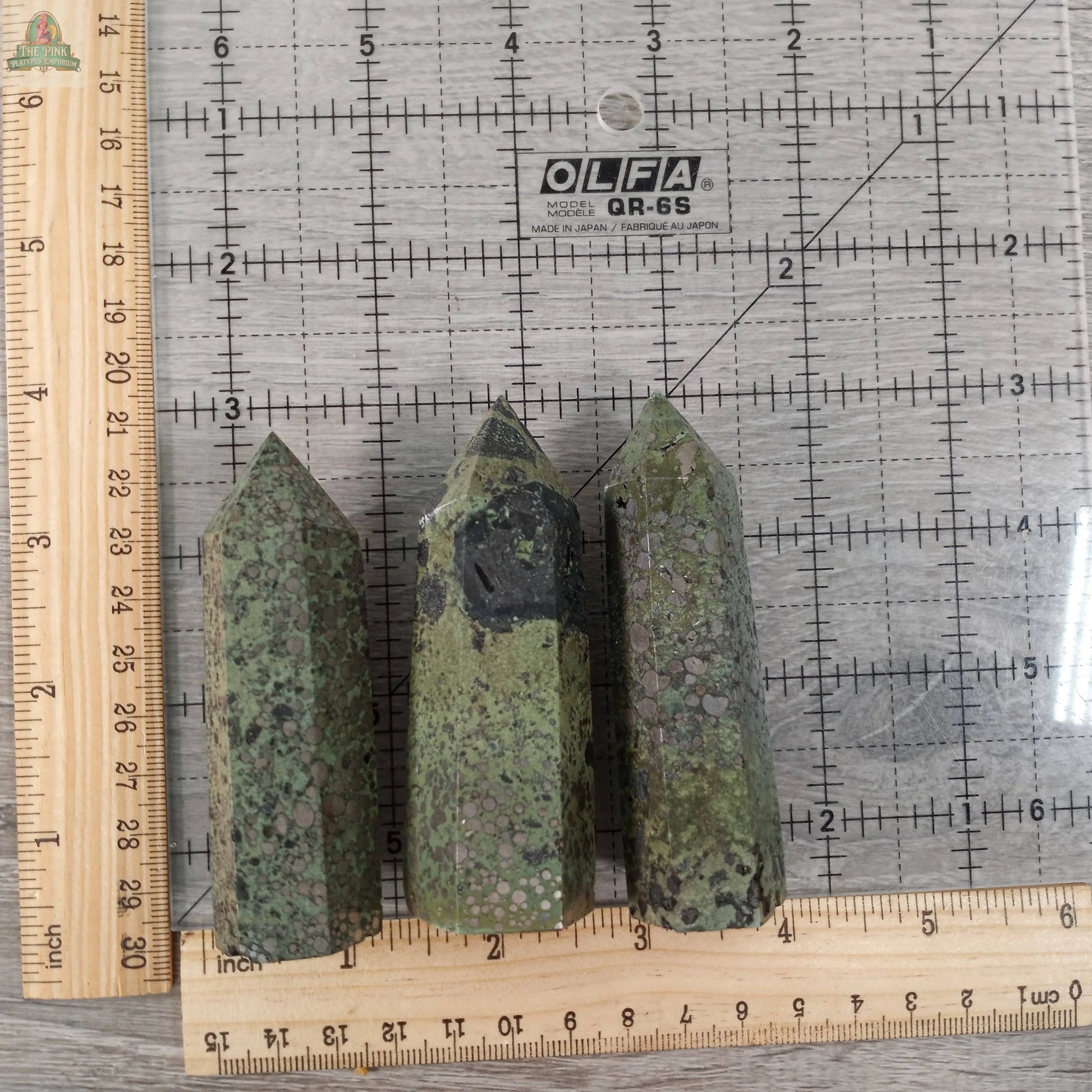 Three Keystone Crystals Gemstone Obelisks – 4 to 5 oz Bulk Crystal Towers Coffee Bean Jasper are upright on a gridded OLFA mat with rulers for scale; each tower measures about 4 to 5 inches tall.
