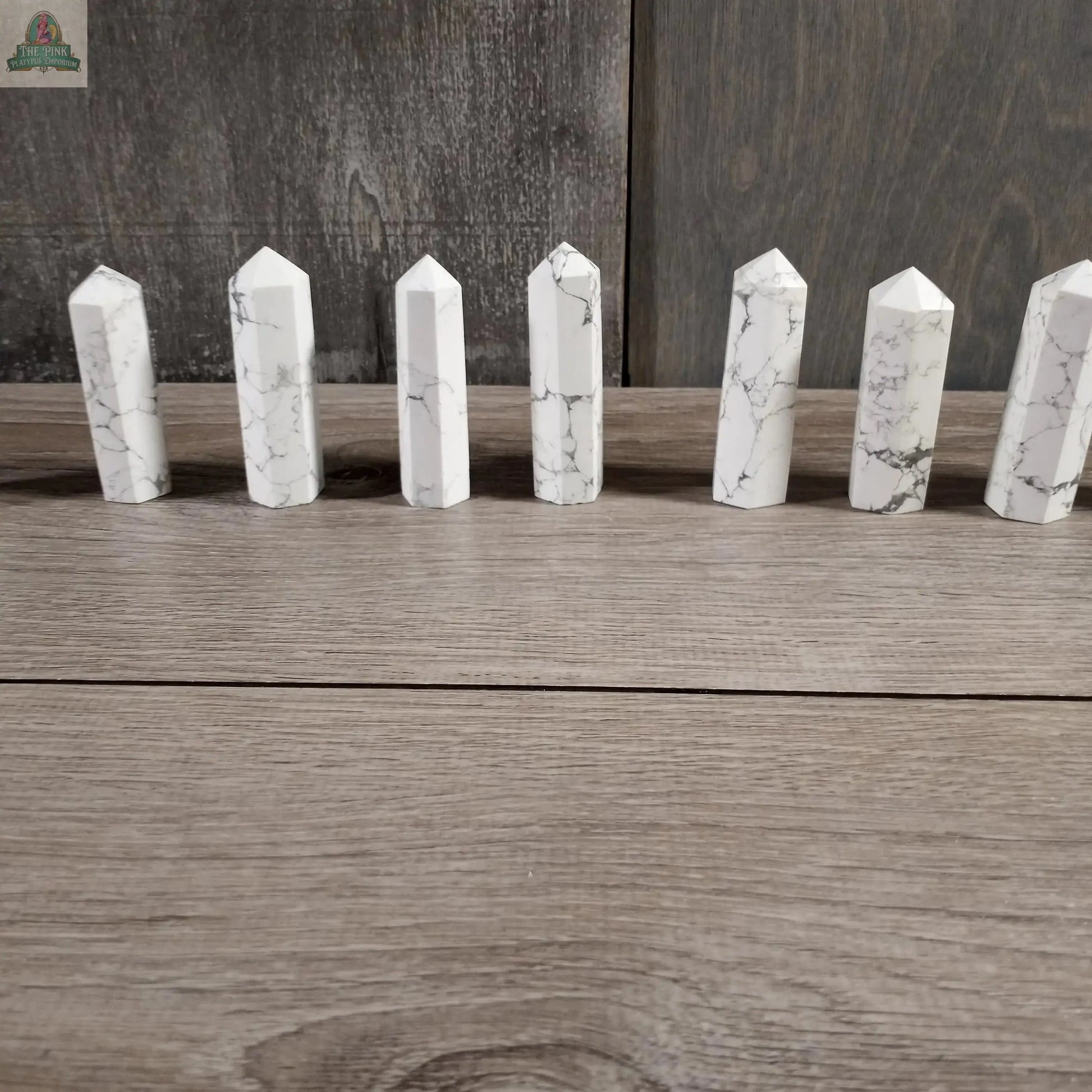 Seven Coffee Bean Jasper crystal obelisks from Keystone Crystals, each weighing 4 to 5 oz, are arranged in a row on a wooden surface with a wood-paneled backdrop.