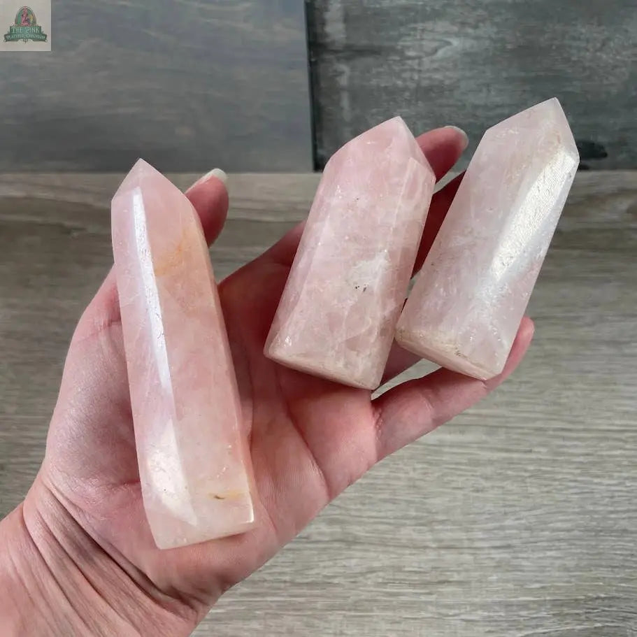 A hand holds three Keystone Crystals Gemstone Obelisks—4 to 5 oz bulk Coffee Bean Jasper crystal towers with pointed tips, displayed against a wooden background.