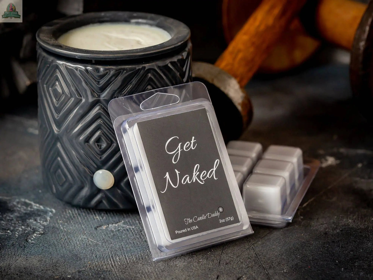 A black ceramic wax warmer sits beside a pack of Get Naked - Mulled Cider & Chestnut Scented Wax Melts, with several white melts taken out and placed on a dark textured surface.