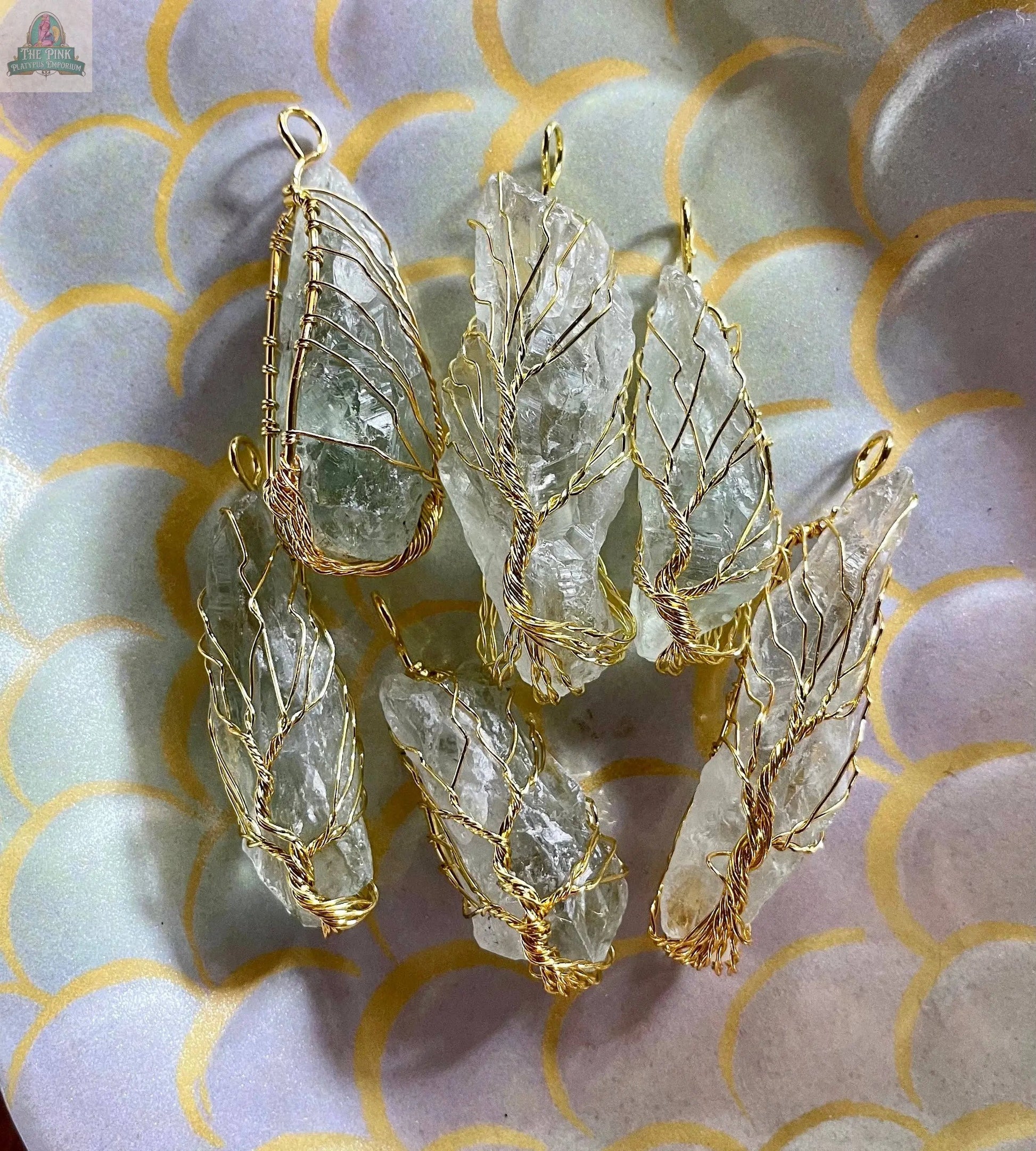 The Golden Wire Wrapped Tree of Life Pendant features clear quartz and prasiolite crystals, artfully arranged on a pastel plate with a scale-pattern of overlapping circles in purple, green, and yellow.