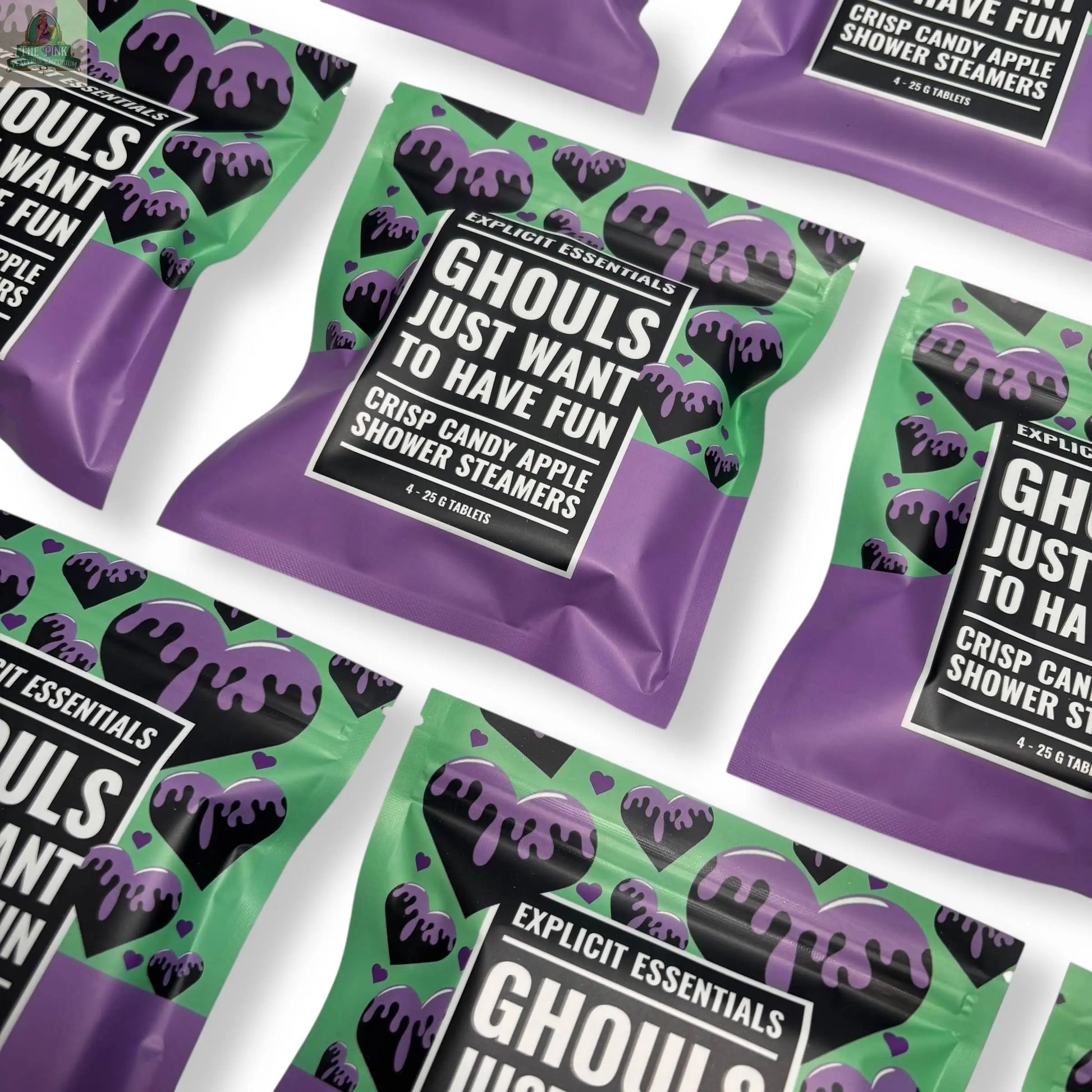 Several green and purple packages of Explicit Essentials Halloween Shower Steamers | Spooky Season Gift, featuring black heart designs with dripping accents, are arranged diagonally on a white surface—perfect for Halloween self-care.