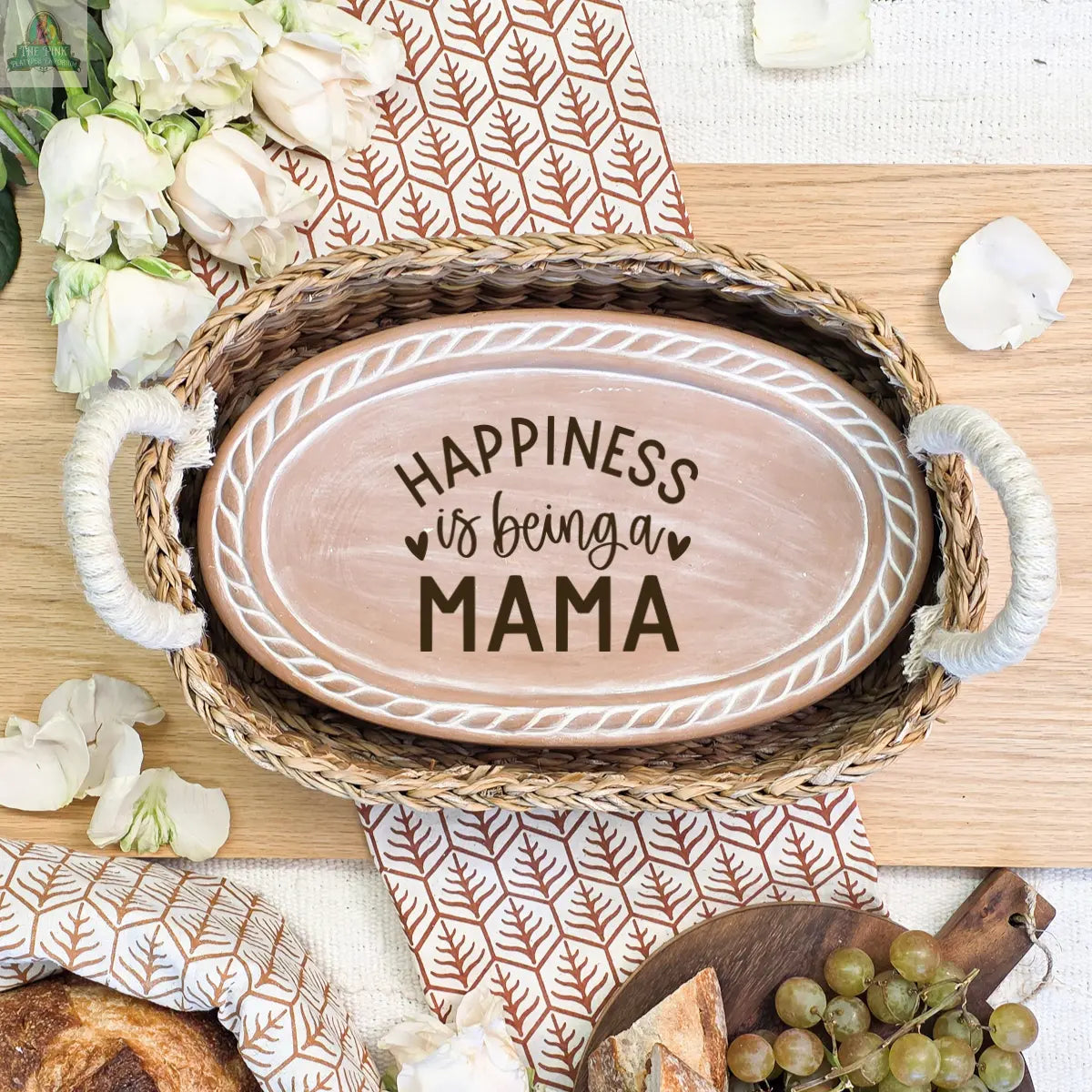 The Handmade Bread Warmer & Wicker Basket - Mom Oval: Design 3 features an oval wooden sign with "Happiness is being a Mama," surrounded by flowers, grapes, dishes—a perfect bread lover's gift on a stylish table runner.