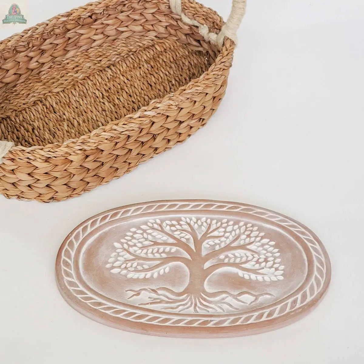 The KORISSA Handmade Bread Warmer & Wicker Basket - Tree of Life Oval features a ceramic plate with a raised white tree design and braided border, nestled in a woven basket with handles—perfect for serving warm bread at your table.
