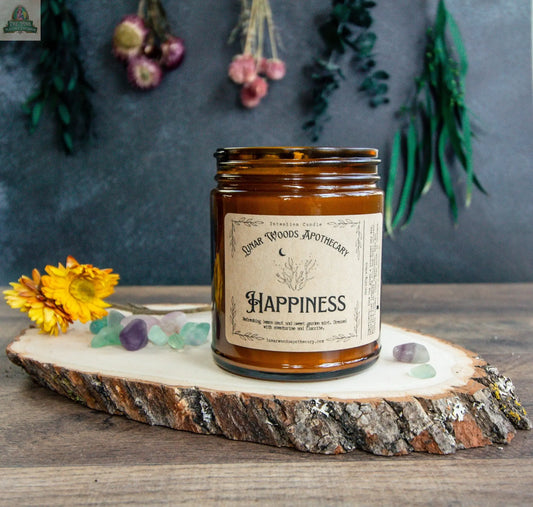 The Happiness candle from Dunar Woods Apothecary sits on a wooden slab, surrounded by yellow flowers and crystals, with dried hanging flowers and greenery in the background.