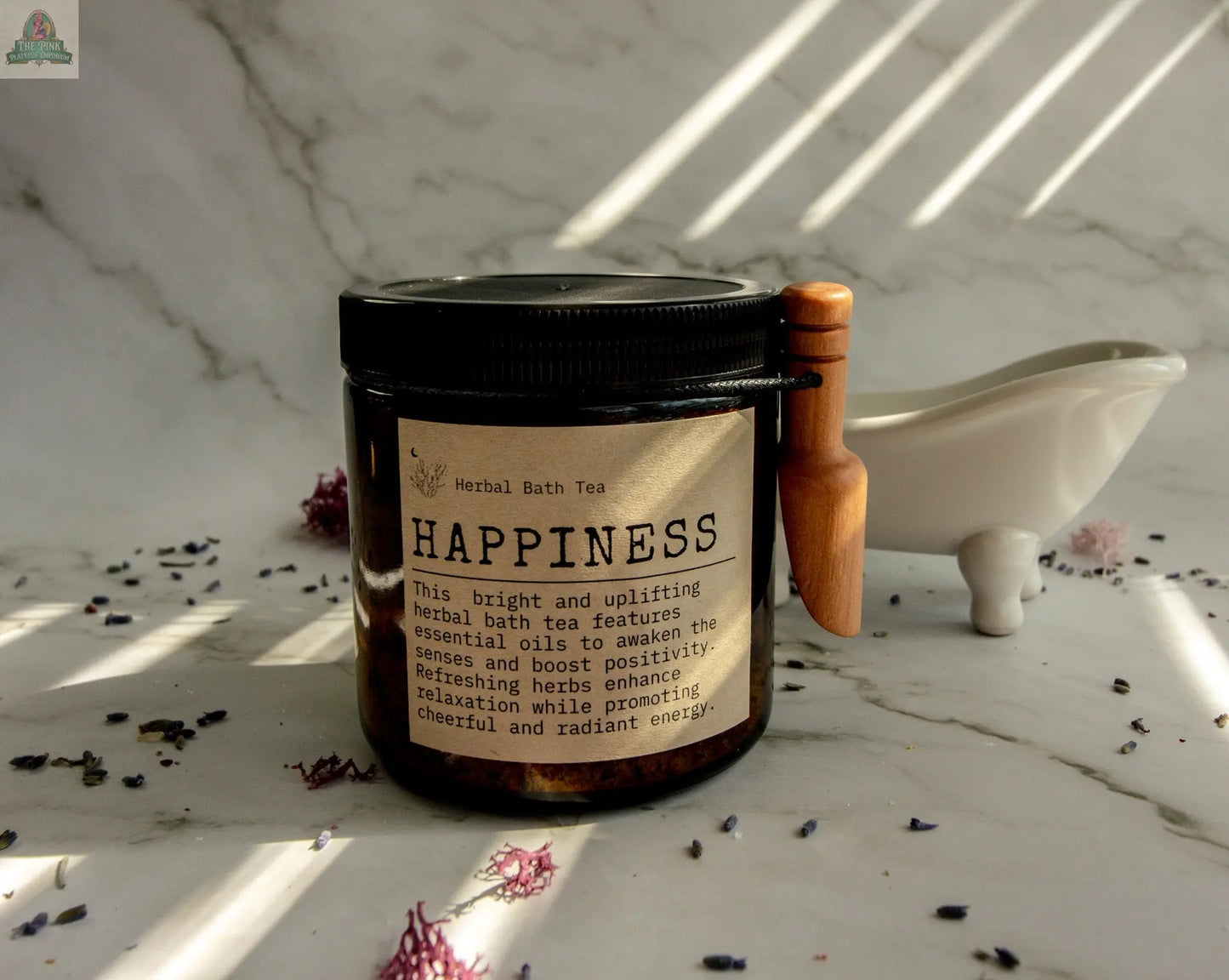 A jar labeled "Happiness" rests on a marble surface with dried herbs nearby, a small white tub, and wooden scoop—ideal for your bath ritual kit. Sunlight streams in, highlighting the serene and inviting setup.