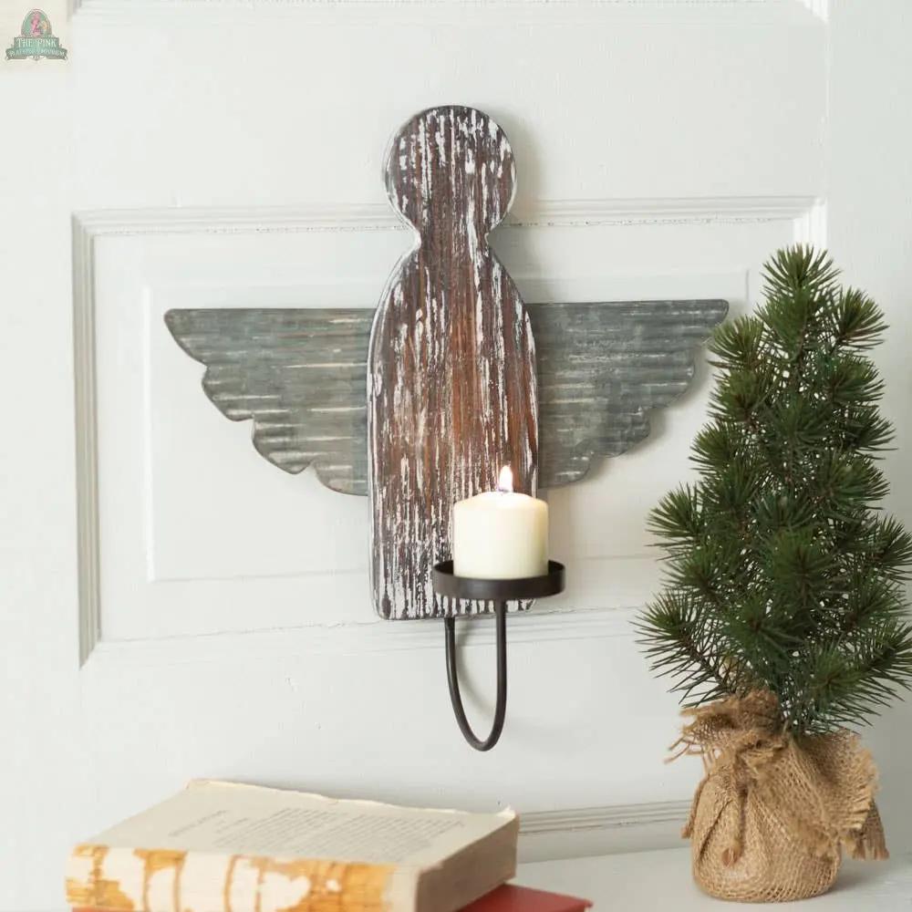 The Heavenly Angel Wall Sconce showcases a distressed wood angel with metal wings holding a white candle, paired with an artificial pine tree in burlap and two vintage books for a charming rustic display.