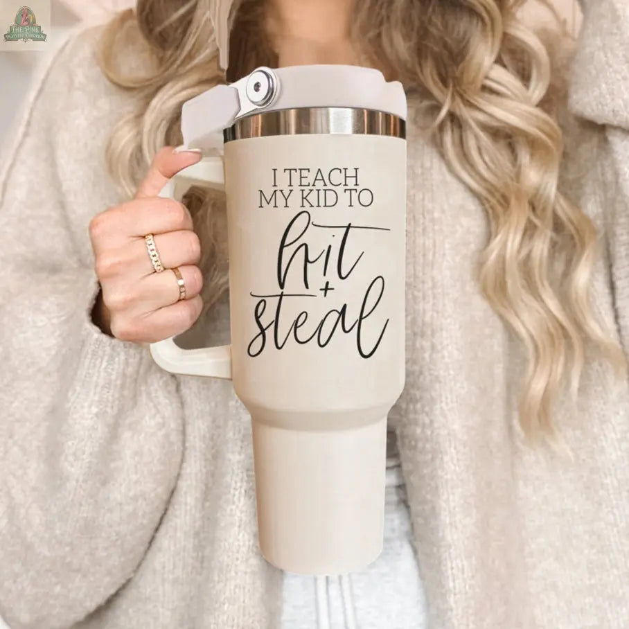 A woman with long wavy blonde hair holds a 40oz Hit & Steal baseball mom tumbler. She wears a beige cardigan and a ring on her finger.