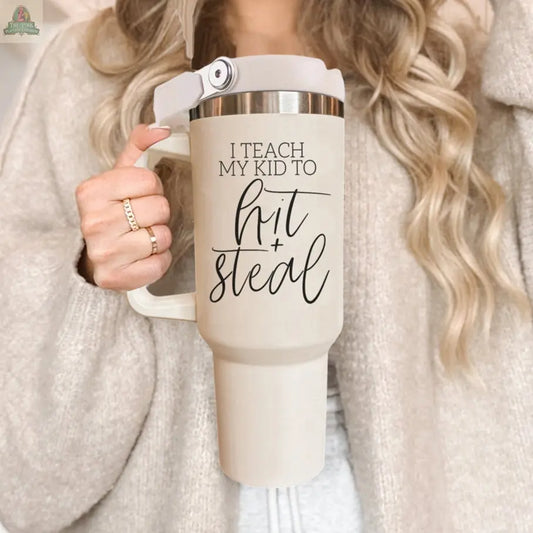 A woman with long wavy blonde hair holds a 40oz Hit & Steal baseball mom tumbler. She wears a beige cardigan and a ring on her finger.