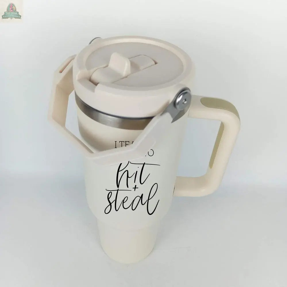 The Hit & Steal is a beige 40oz tumbler travel mug with a large handle and lid. It features "I Teach My Kid to Hit + Steal" in black cursive on the side—perfect for any baseball mom! Background is plain white.
