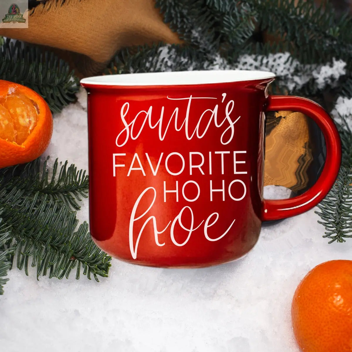 The Ho Ho Hoe Mug is a red ceramic campfire mug with "Santa’s Favorite Ho Ho Hoe" in white script. Surrounded by evergreen and oranges on snow, this handmade mug is microwave safe and perfect for gifting.