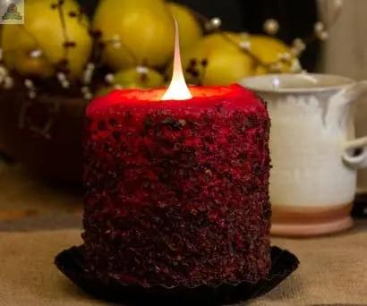 A glowing Homespun Harvest Electric Candle rests on a black tray, with a blurred background of yellow apples and a ceramic mug.