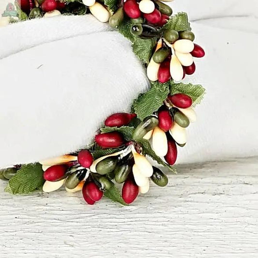 The ISB13700FH 1.5in Pip Berry Taper Ring/Napkin Ring features artificial red, green, and cream berry beads with green fabric leaves—perfect farmhouse decor for your table, displayed on a light-colored surface.