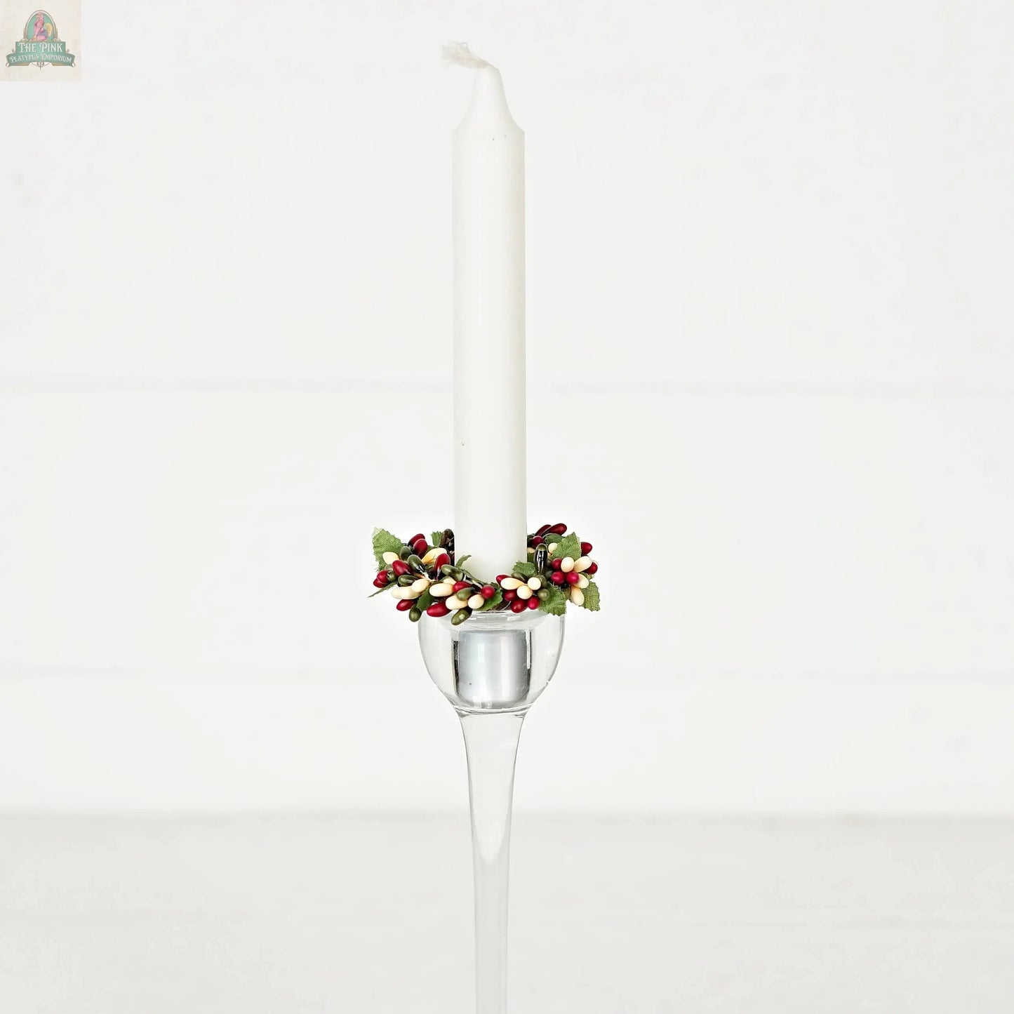 The ISB13700FH 1.5in Pip Berry Taper Ring/Napkin Ring-Farmhouse features red, white, and green artificial berries and leaves on a white taper candle in a clear glass holder—perfect farmhouse décor on a plain white background.