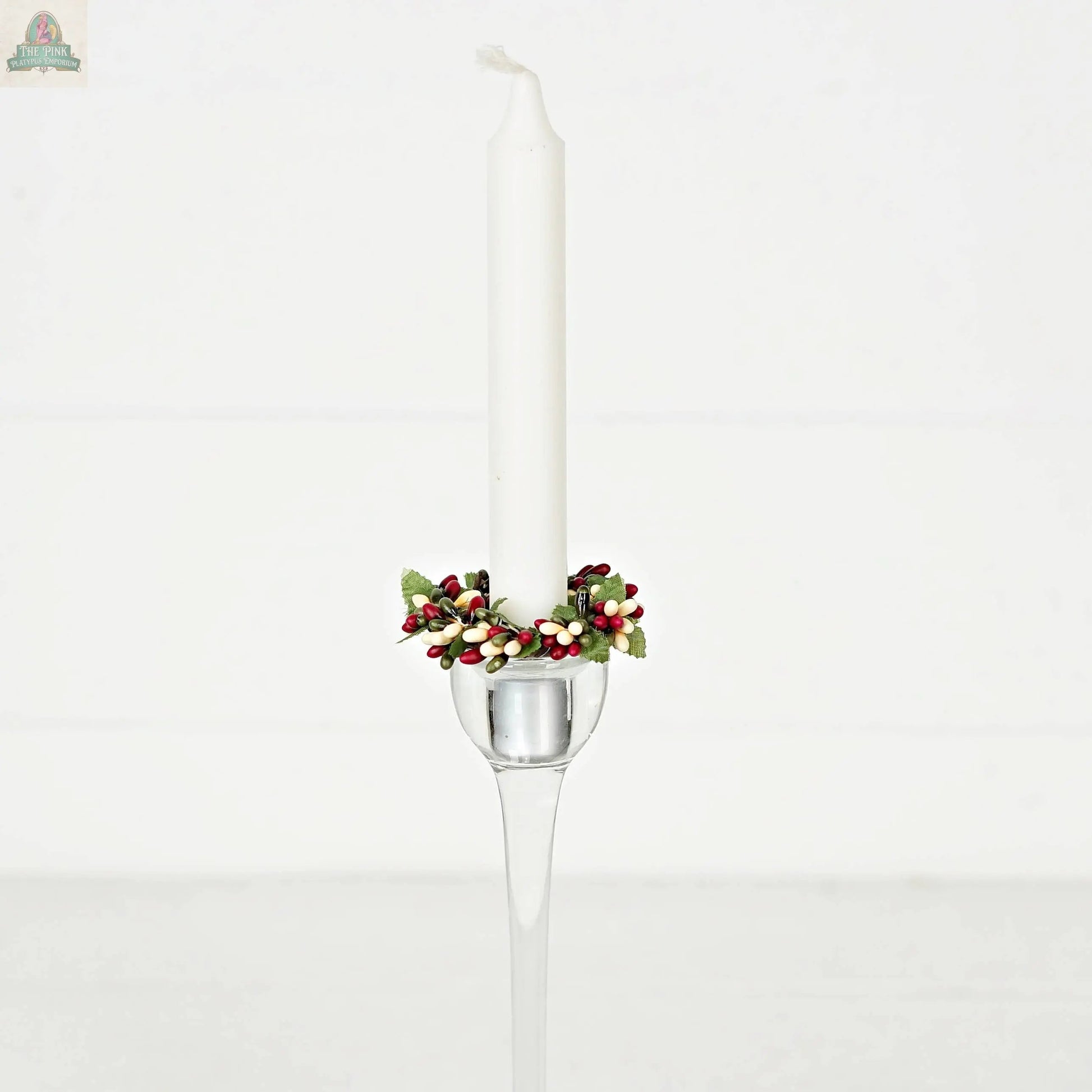 The ISB13700FH 1.5in Pip Berry Taper Ring/Napkin Ring-Farmhouse features red, white, and green artificial berries and leaves on a white taper candle in a clear glass holder—perfect farmhouse décor on a plain white background.