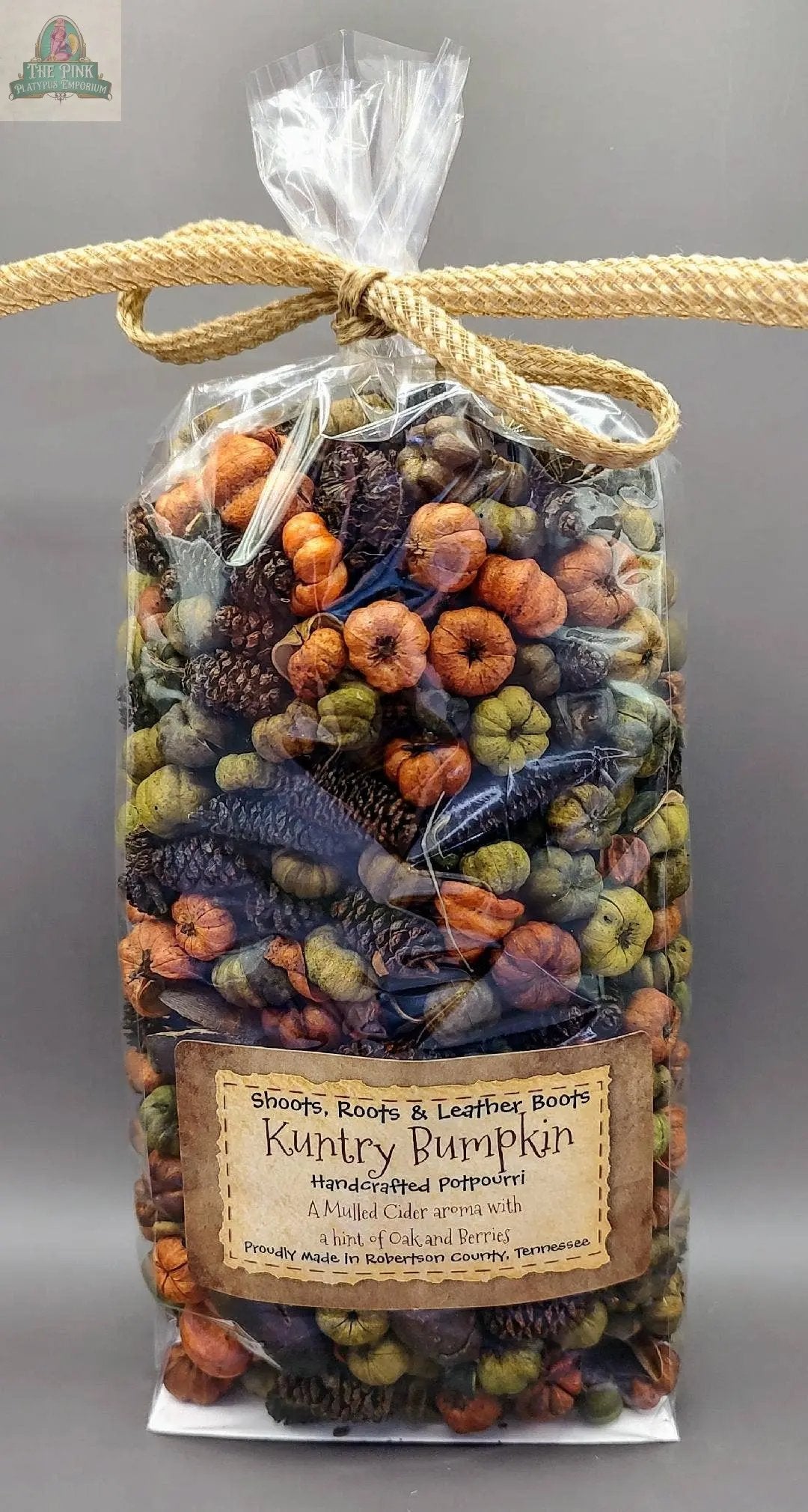 A clear plastic bag of Kuntry Bumpkin Handcrafted Potpourri- 5 cups, featuring orange, green, and brown pieces, is tied with a tan rope. This colorful potpourri makes a perfect home fragrance accent.