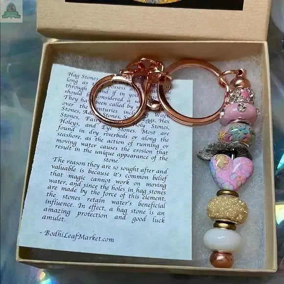 The Lady of The Moon Gift Box features a beaded keychain with rose gold hardware, colorful beads including a heart and genuine hag stone, displayed on an info card about Sanibel Island hag stones and their magical properties.