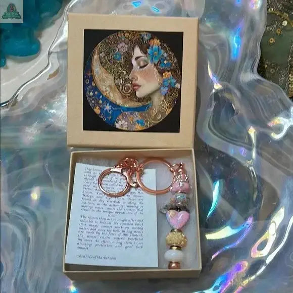 The Lady of The Moon Gift Box features a floral portrait of a woman on the lid. Inside are a hagstone beaded keychain, a note, and decorative beads. The box evokes Sanibel Island’s coastal charm with its iridescent, wavy surface.