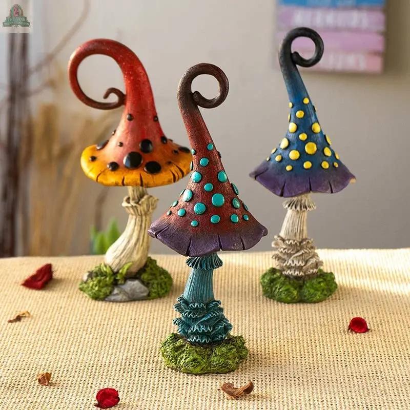 Add cottagecore charm to your space with the Magic Toadstool Mushrooms Home and Garden Decor—three whimsical, colorful statues with curly tops and polka dots, set on a textured base with grass accents and scattered flower petals.