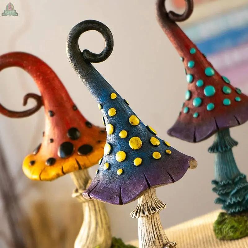 Add a cottagecore vibe to your space with Magic Toadstool Mushrooms Home and Garden Decor—three whimsical statues in red, blue, and purple with twisted caps and vibrant spots. Charming indoors or outdoors; displayed against a blurred background.