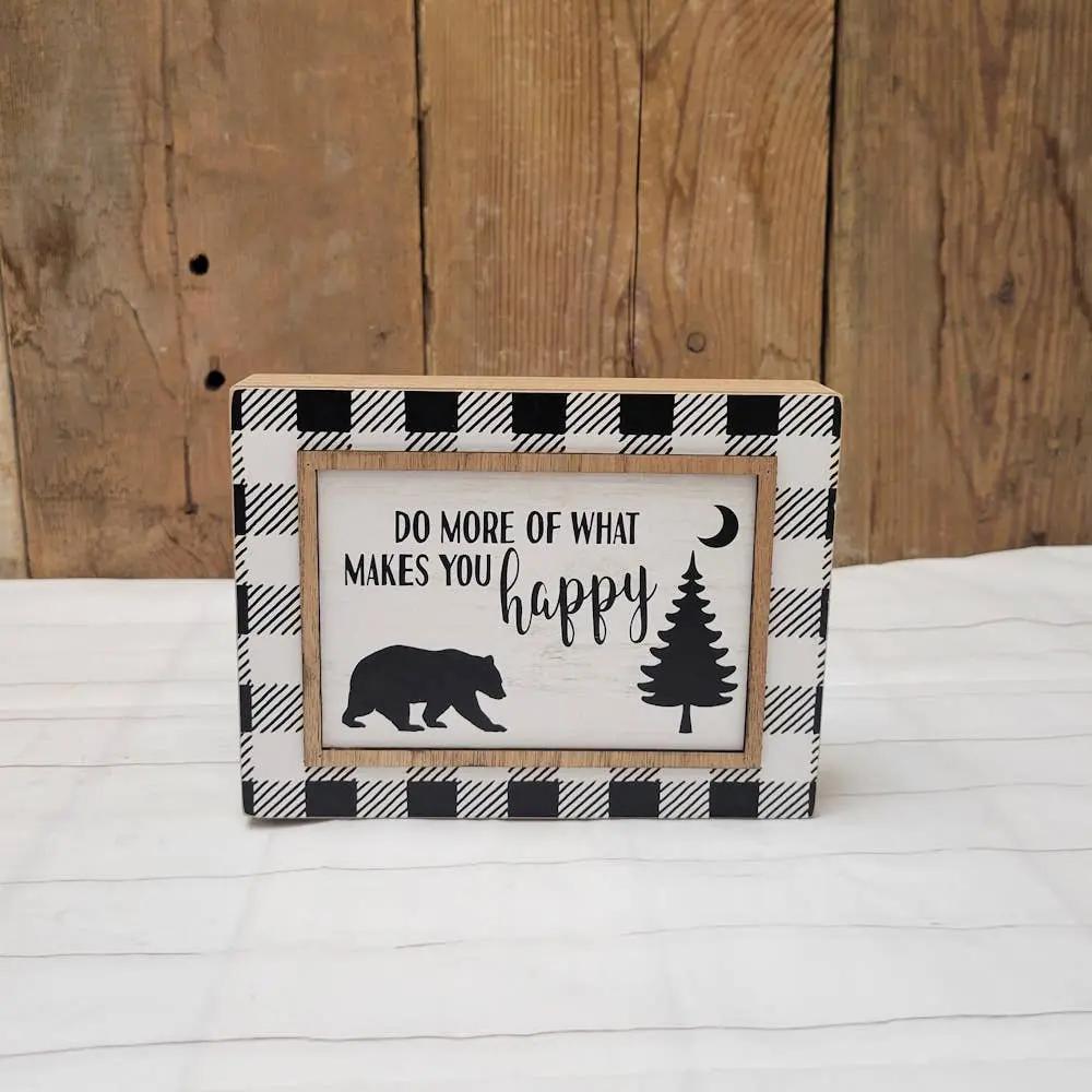 Add a cozy touch to your home with the Makes You Happy Sign, featuring a rustic wood background, black-and-white plaid border, bear, pine tree, crescent moon silhouettes, and the uplifting message “DO MORE OF WHAT MAKES YOU happy.”.