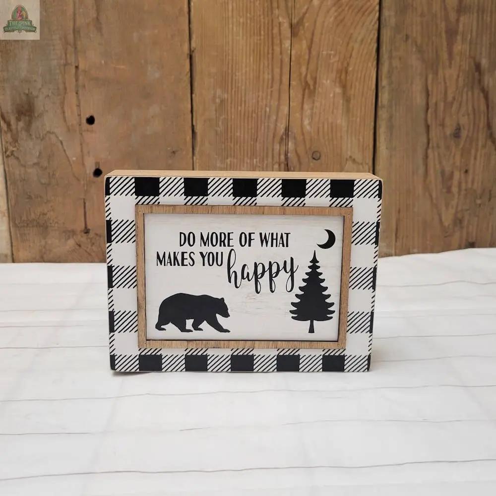 Add a cozy touch to your home with the Makes You Happy Sign, featuring a rustic wood background, black-and-white plaid border, bear, pine tree, crescent moon silhouettes, and the uplifting message “DO MORE OF WHAT MAKES YOU happy.”.