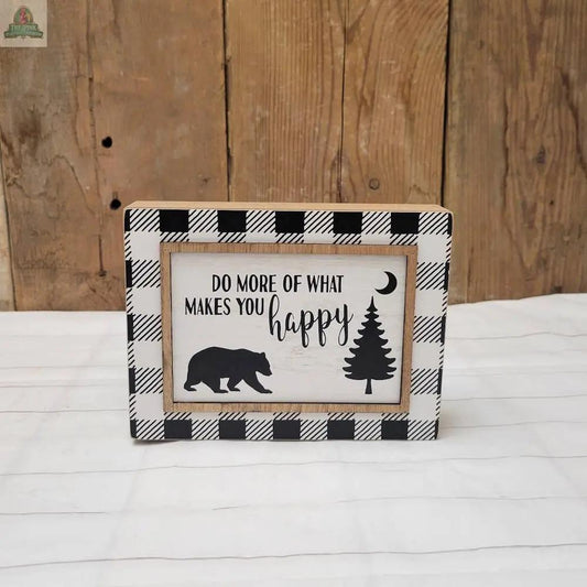 Add a cozy touch to your home with the Makes You Happy Sign, featuring a rustic wood background, black-and-white plaid border, bear, pine tree, crescent moon silhouettes, and the uplifting message “DO MORE OF WHAT MAKES YOU happy.”.