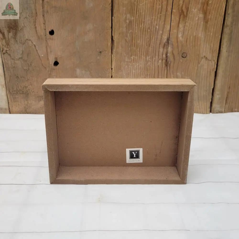 The Makes You Happy Sign—a simple wooden shadow box frame with a small label—rests on a white surface against a rustic wooden wall, perfect as unique home decor or a one-of-a-kind wall hanging sign.