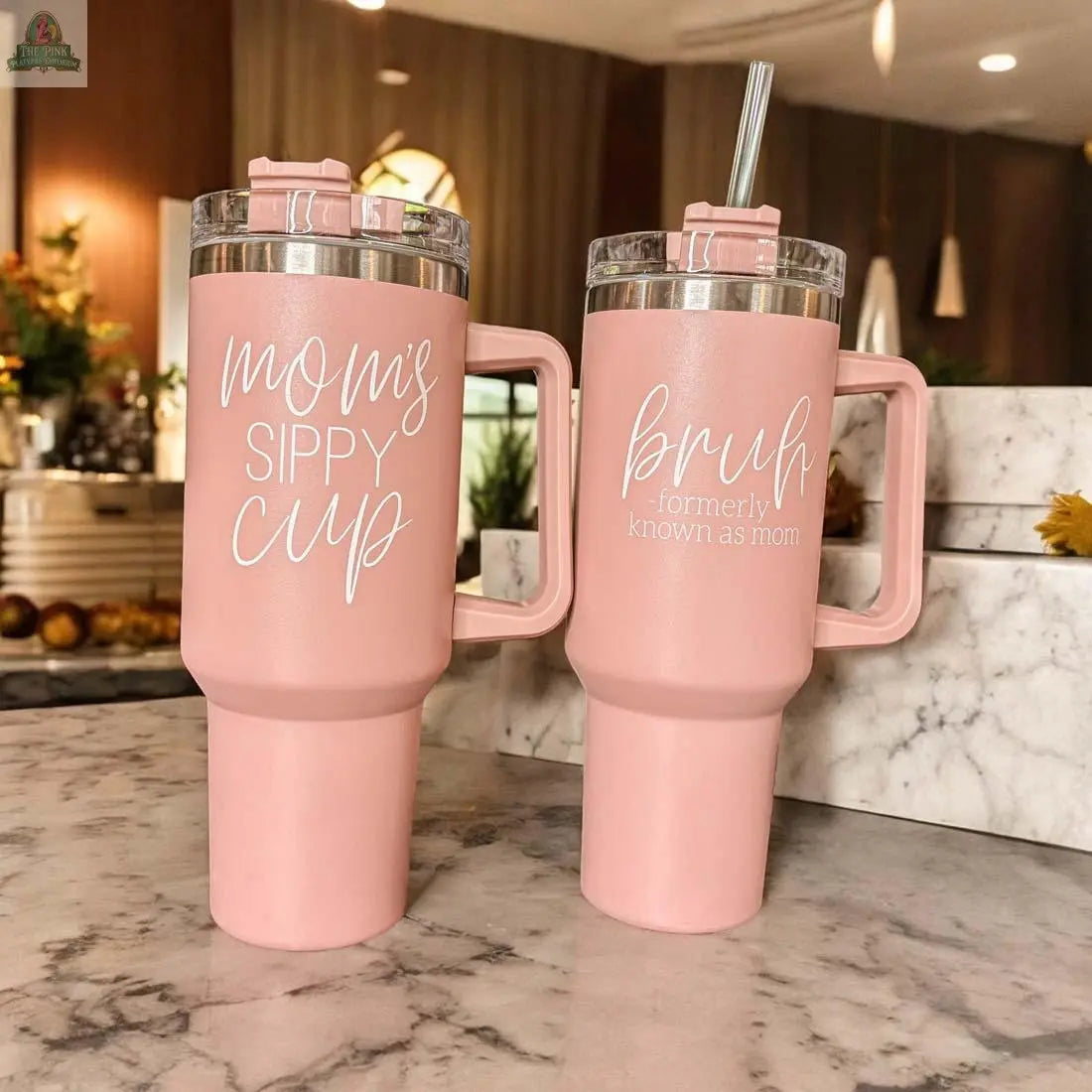 Two pink Mom's Sippy 40oz tumblers with handles rest on a marble counter. One says “mom’s sippy cup,” the other “bruh - formerly known as mom,” and both add a playful touch to any cozy kitchen.