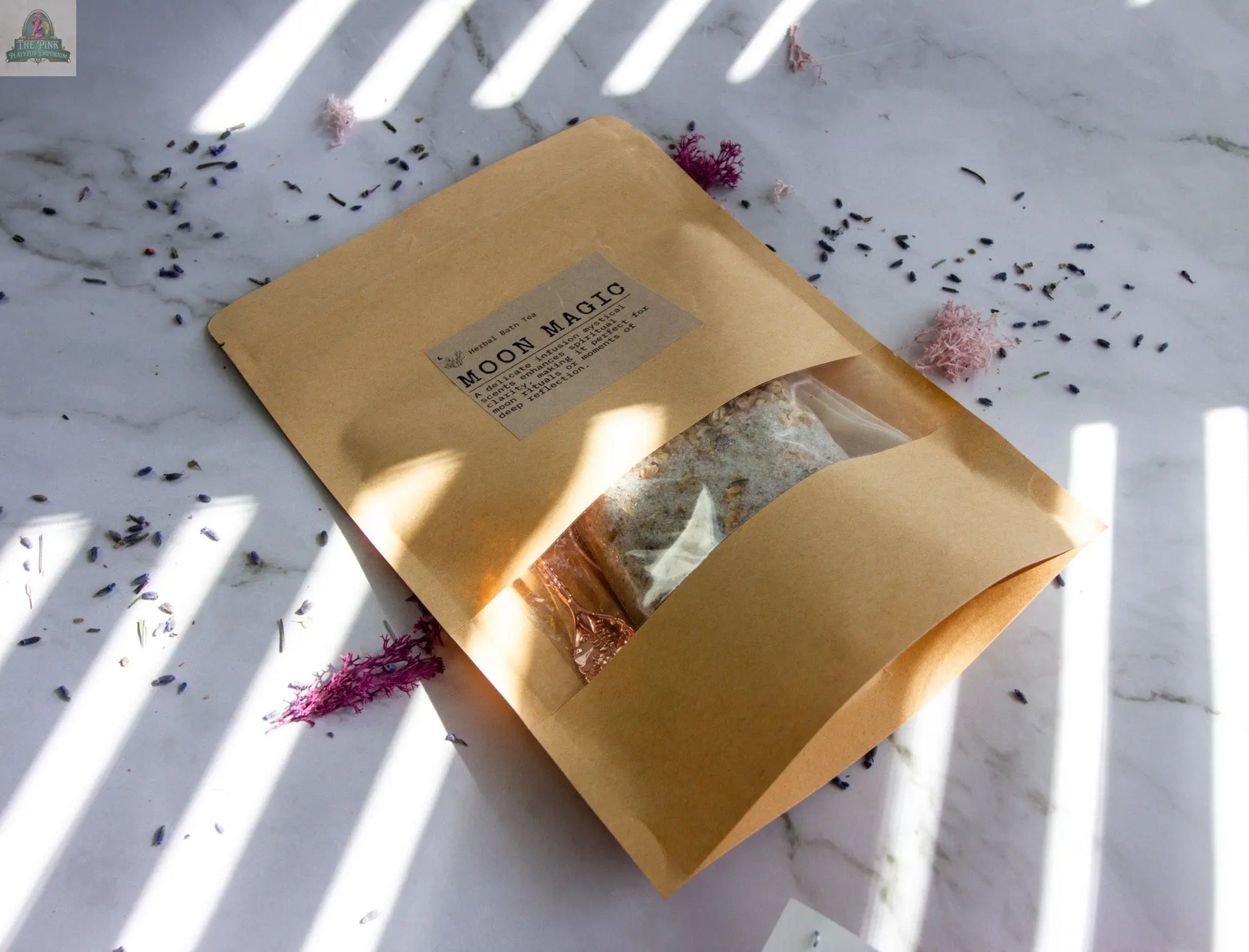 A brown paper package labeled Moon Magic rests on marble, surrounded by dried flowers and lavender—ideal for moon rituals or a calming herbal bath tea infused with jasmine and vanilla essential oils, touched by sunlight.