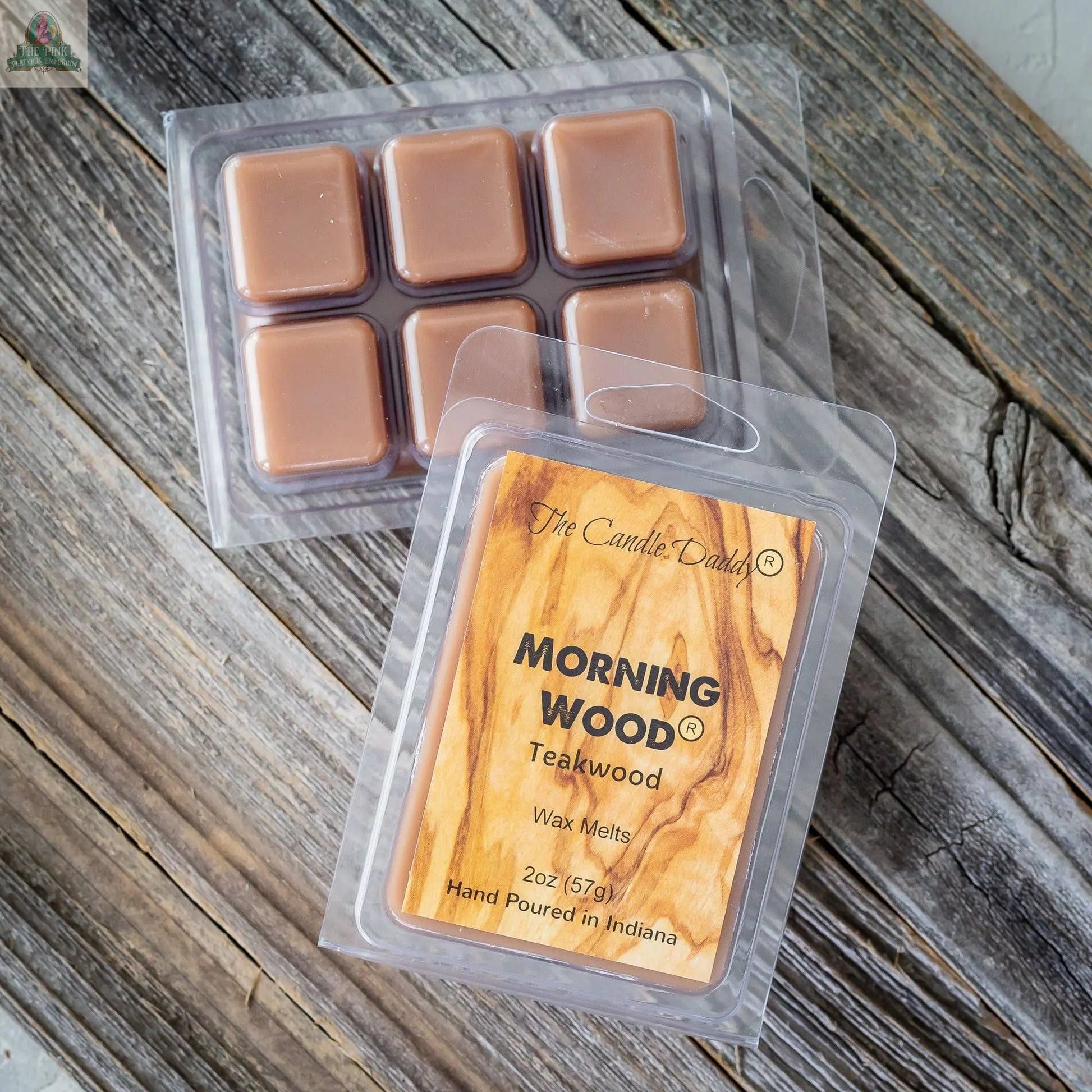 Two clamshell packs of Candle Daddy wax melts sit on wood. One is open with six brown cubes; the other shows the label "Morning Wood - Teak Wood Scented Wax Melt," known for its strong fragrance, hand poured in Indiana.