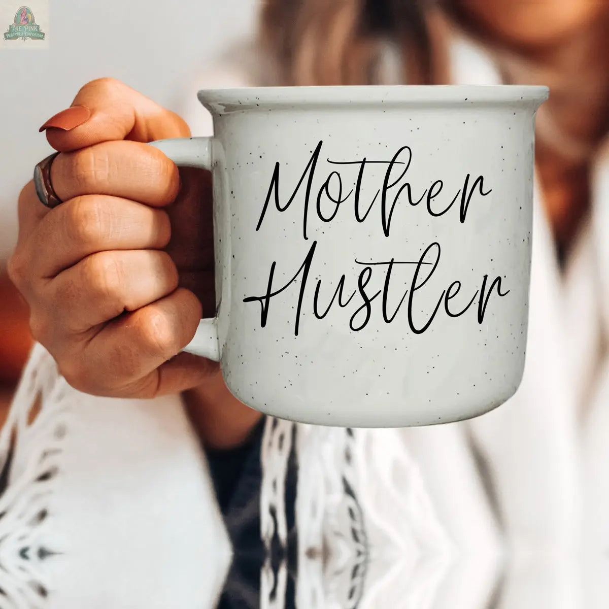 A person holds the 14.5oz Mother Hustler mug, featuring "Mother Hustler" in black script against light gray—a stylish, motivational coffee mug moment. Only their hand and part of their upper body are visible.