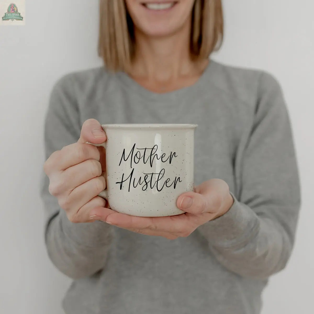 A woman in a gray sweater smiles while holding the Mother Hustler 14.5oz mug, featuring “Mother Hustler” in black script.