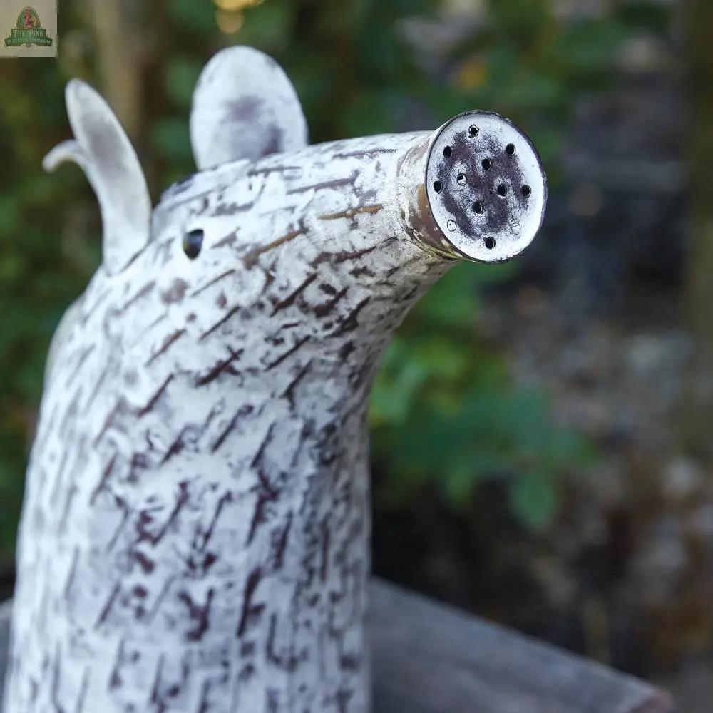 A close-up of the Mouse Watering Can, a charming garden accessory shaped like a mouse with painted fur and a spout-shaped snout, sits on display against a backdrop of blurred greenery.