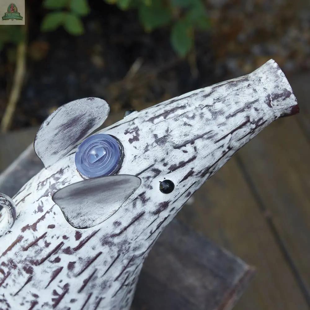 Close-up of the Mouse Watering Can, a rustic ceramic sculpture in white and brown with a long snout, upright ears, and a spiral eye, displayed on a wooden outdoor surface.