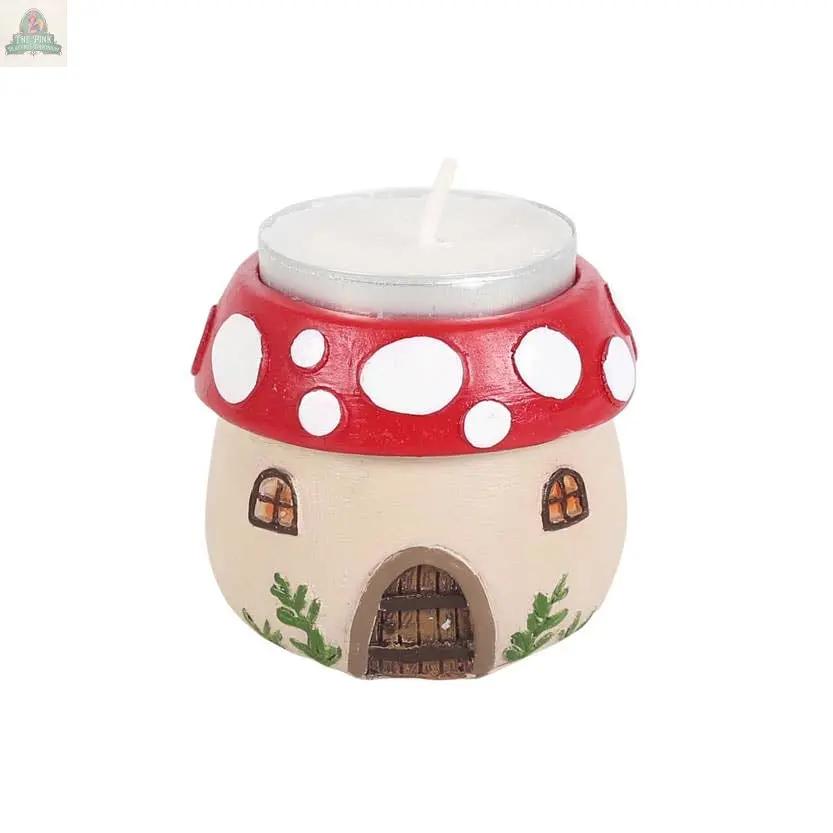 The Mushroom House Resin Tealight Holder features a beige stem, red cap with white spots, tiny windows, a door, and green accents—making it a charming gift or whimsical addition to cozy winter or forest-themed home decor.