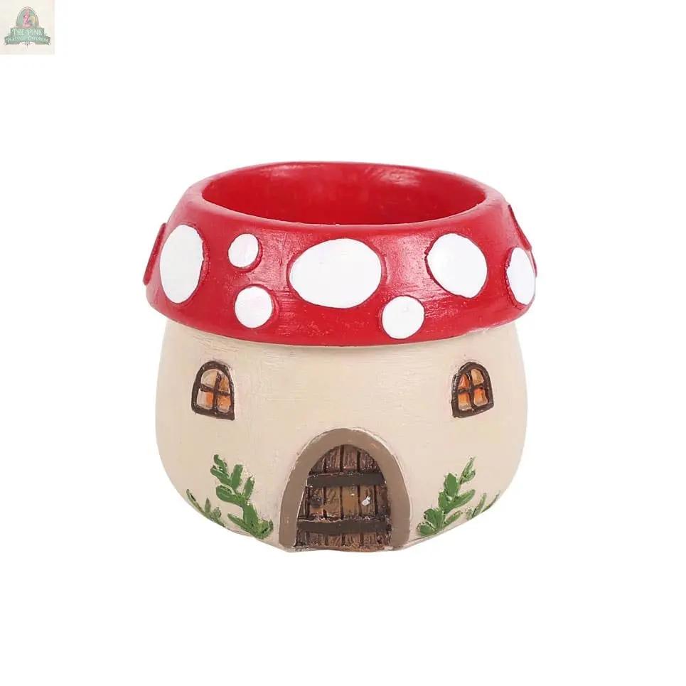 A whimsical Mushroom House Resin Tealight Holder with a red top, white spots, windows, brown door, and green leaf base—perfect winter forest decor or a charming gift for gnome lovers.