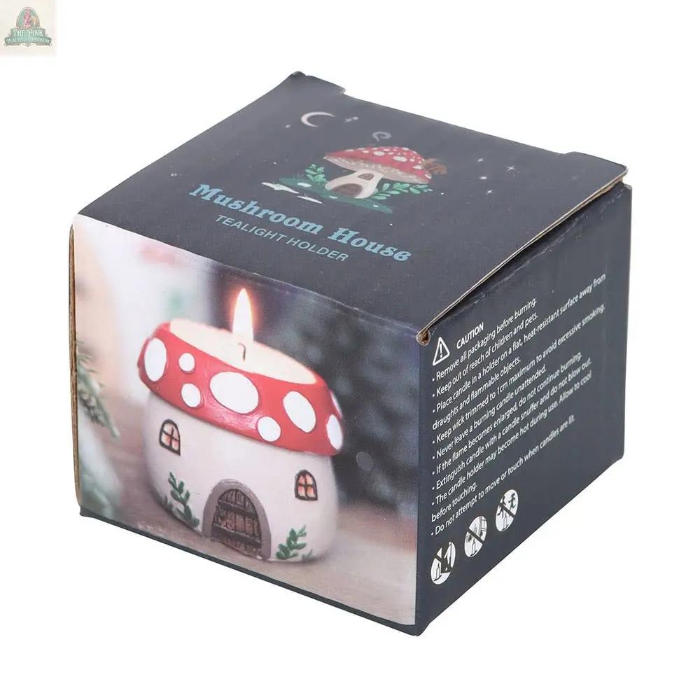 A box labeled Mushroom House Resin Tealight Holder shows an illustration and photo of a red and white mushroom-shaped candle holder with windows, door, and glowing tealight—ideal for winter décor or gnome gifts. Caution instructions included.