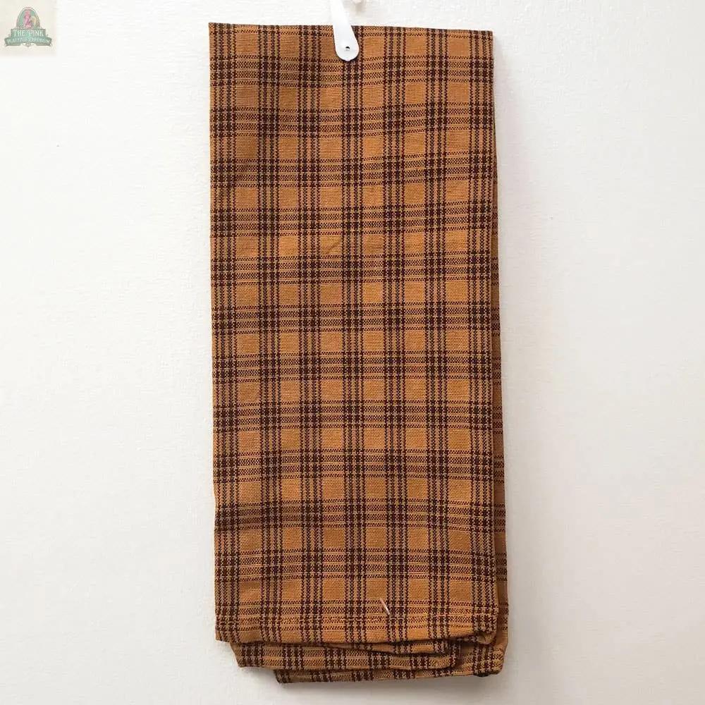 A folded Mustard Kitchen Towel with thin black lines hangs on a white hook against a white wall.
