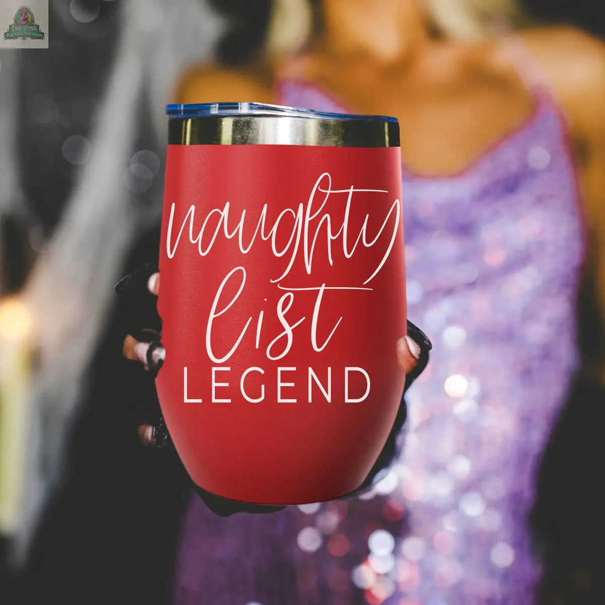 A person in a sparkly purple outfit holds the Naughty List 17oz red stainless steel tumbler, featuring "naughty list LEGEND" in white script. The background is blurred.