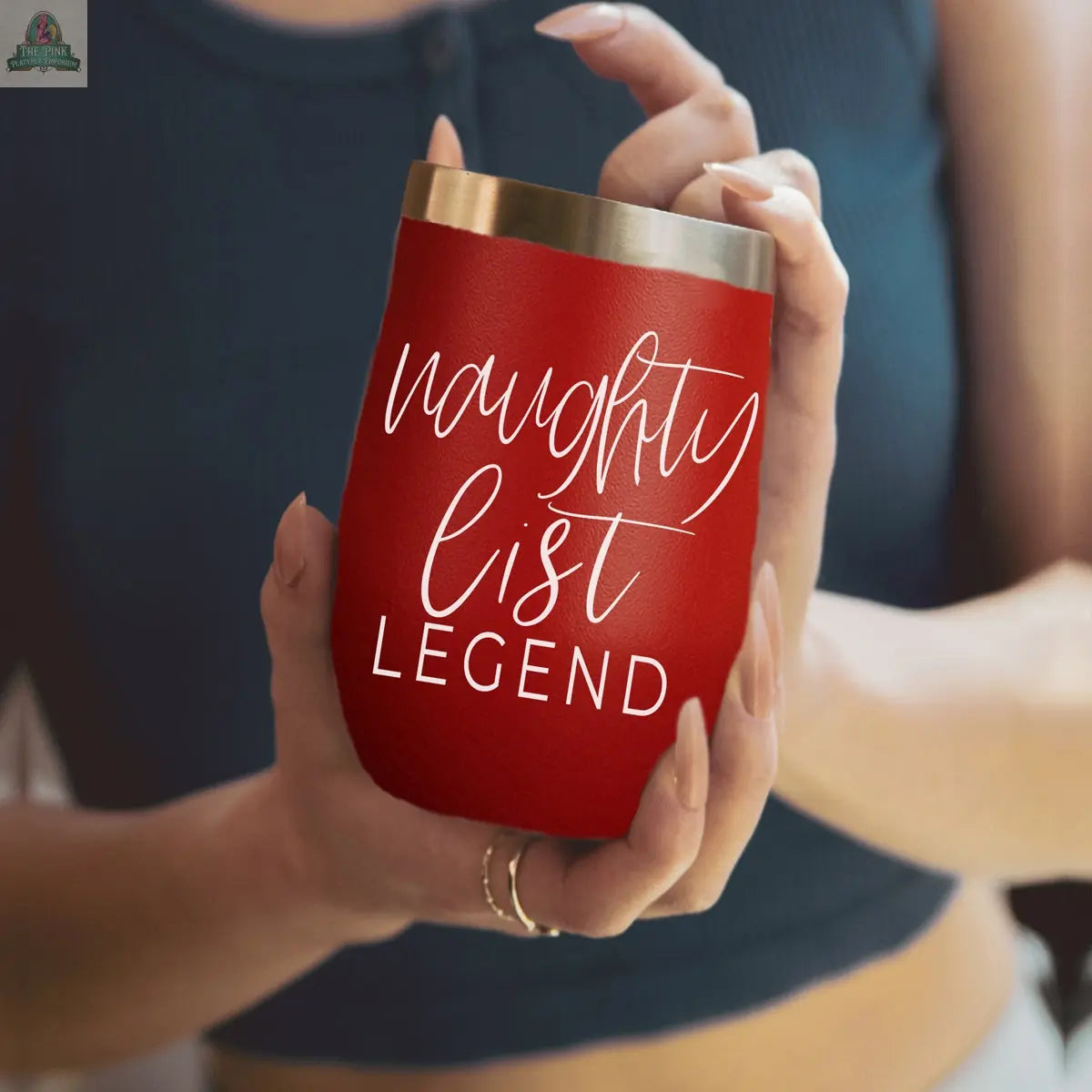 A person in a blue top holds a red Naughty List 17oz tumbler with “naughty list LEGEND” written in white script.