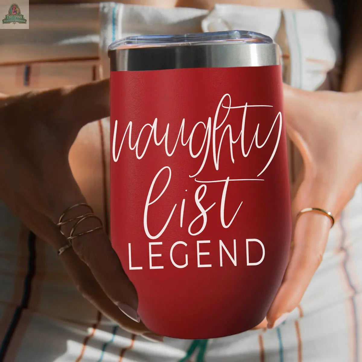 A person holds the Naughty List 17oz red stainless steel tumbler with “naughty list LEGEND” in white lettering, wearing rings and striped clothing.