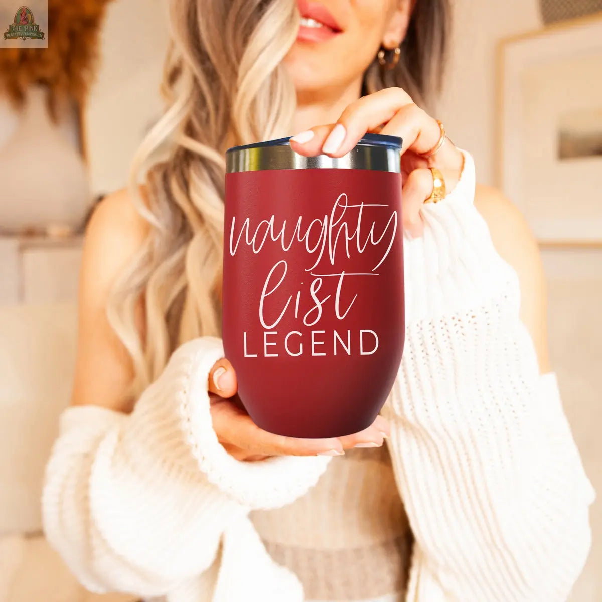 A smiling woman with long, wavy hair holds the 17oz Naughty List tumbler, featuring "naughty list LEGEND" in white script. She wears a cozy white sweater.