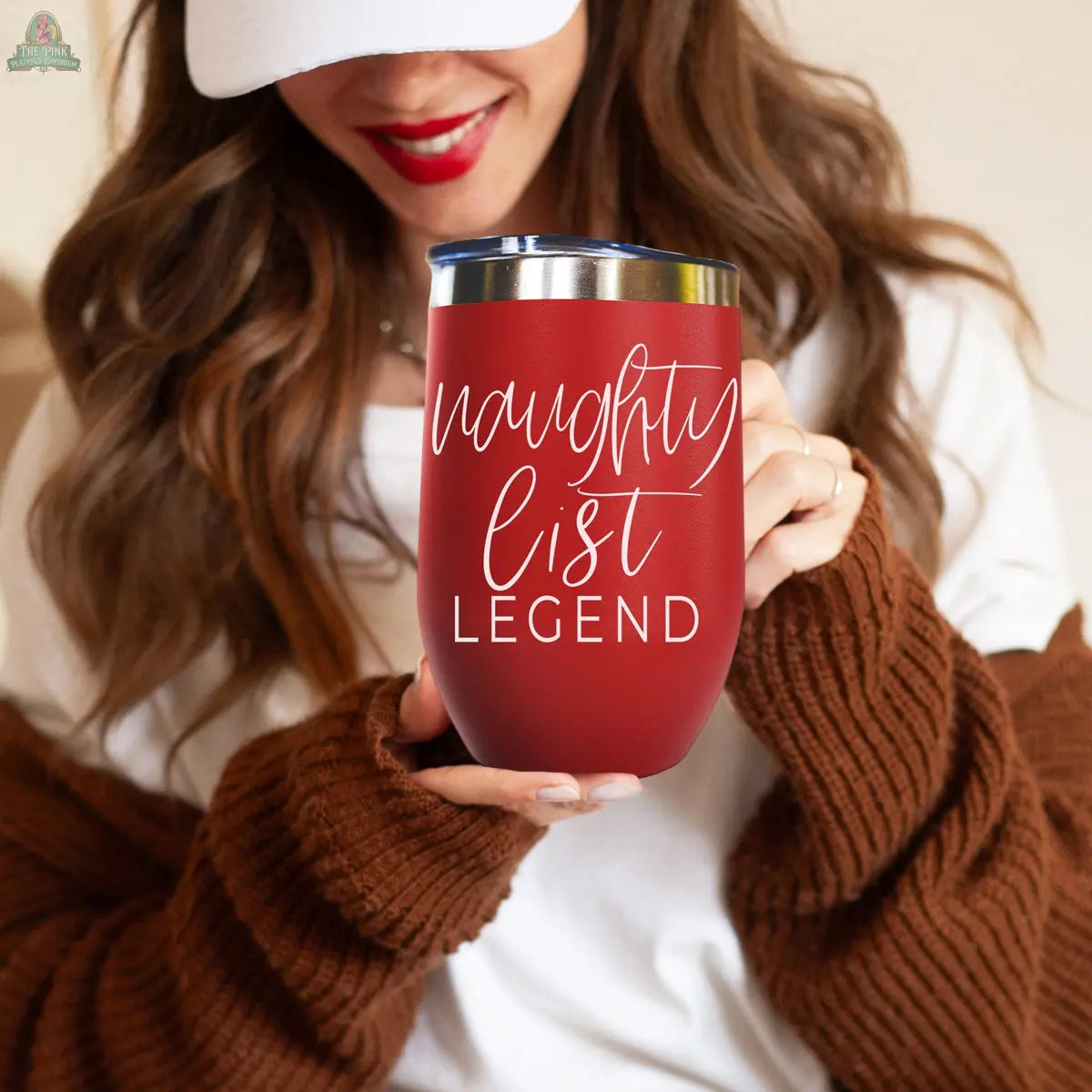 A woman in a white shirt and brown sweater smiles while holding the Naughty List 17oz red stainless steel tumbler featuring "naughty list LEGEND" in white script.