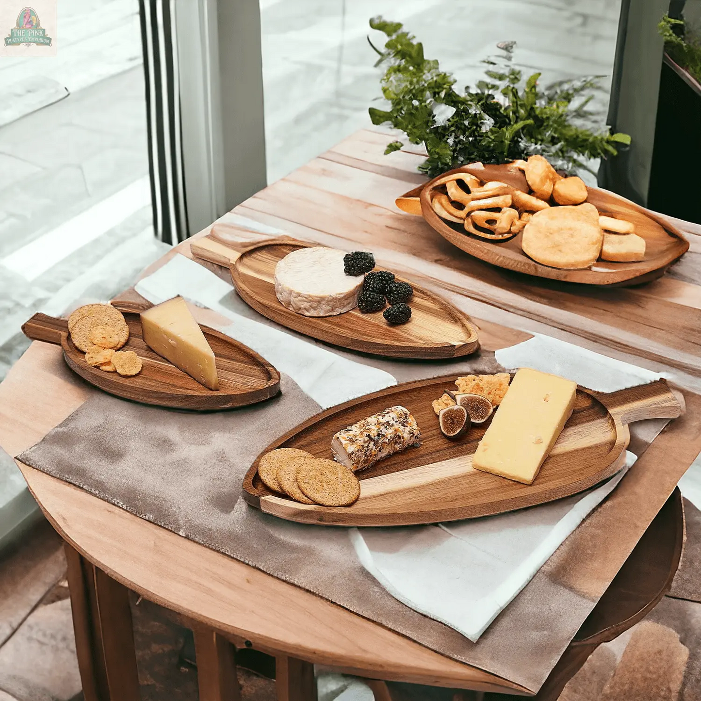 A wooden table displays cheese board essentials—crackers, cheeses, blackberries, and figs—on Nesting Trays | 3 Sizes, made of acacia wood, near a sunlit window with a potted plant in the background.