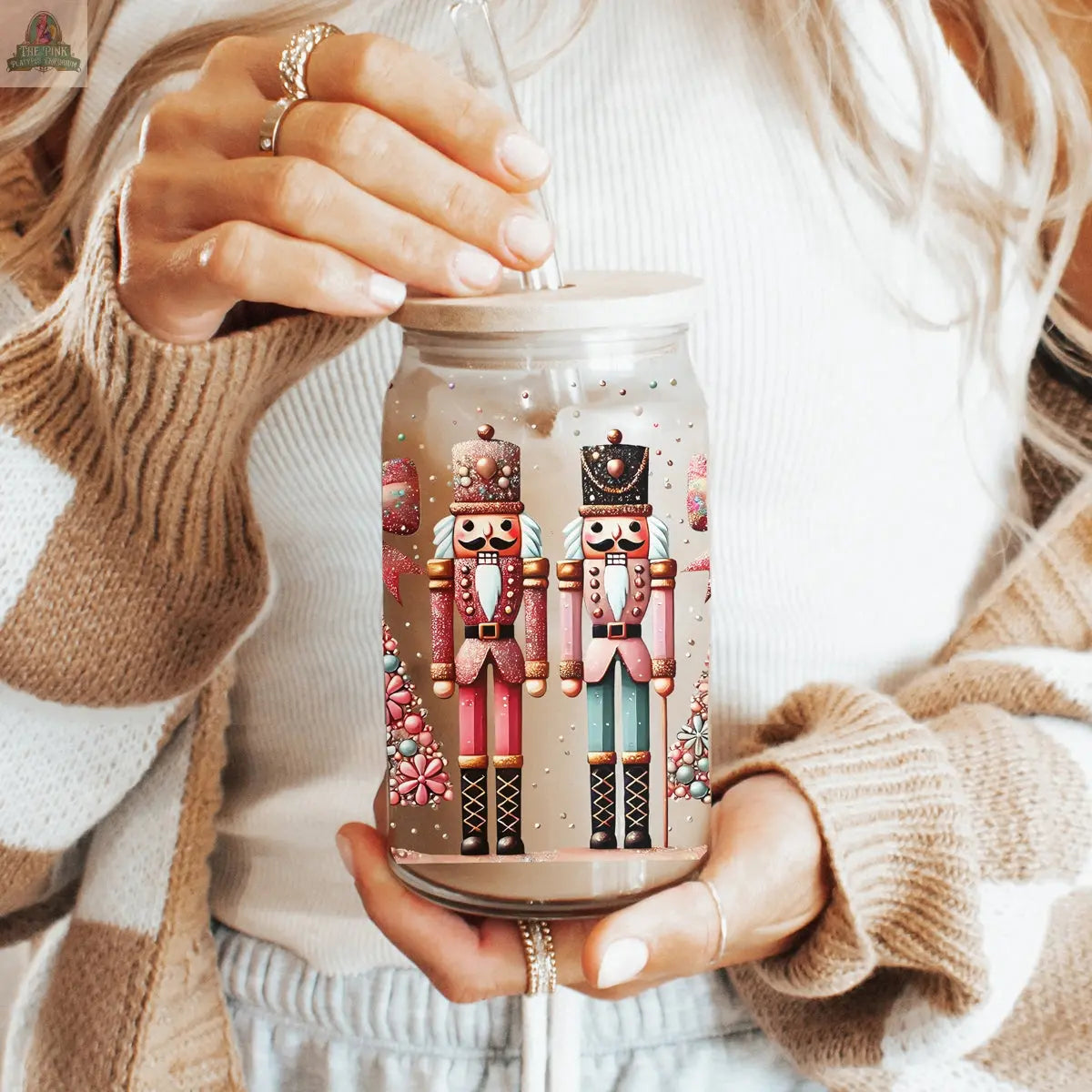 A woman in a white top and brown striped sweater holds the Nutcracker Glam Soldier tumbler, a festive holiday drinkware featuring vibrant nutcracker illustrations and enchanting Christmas designs.