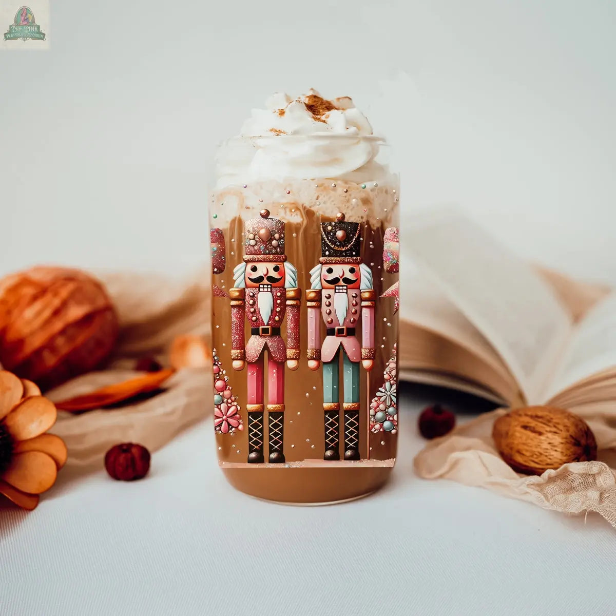 Enjoy a cozy glass of coffee topped with whipped cream and festive nutcracker designs. Surrounded by autumn decor, flowers, nuts, and an open book, the scene highlights the charming Nutcracker Glam Soldier tumbler.