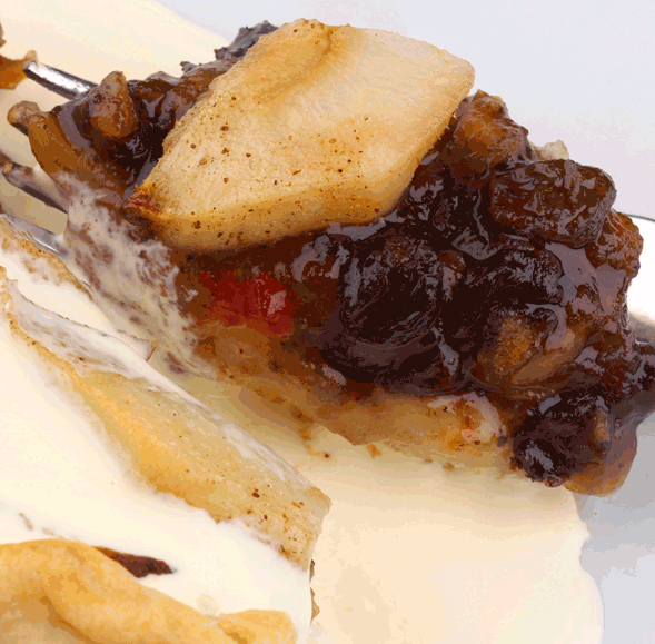 A close-up of a slice of fruit pie with dark fruits, nuts, and baked apples, served with melting whipped cream—evoking the cozy aroma of Nutmeg & Cream Atomizer Oils in the air.