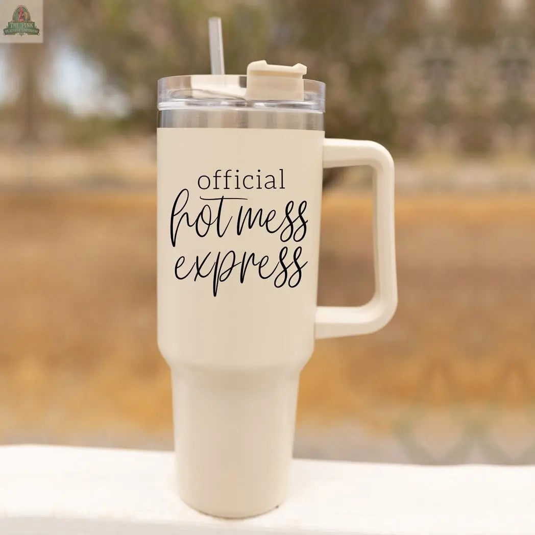 The Official Hot Mess 40oz is a large, cream-colored insulated tumbler with a handle, clear lid, and straw. The cup features “Official Hot Mess Express” in black script and regular fonts on its surface.