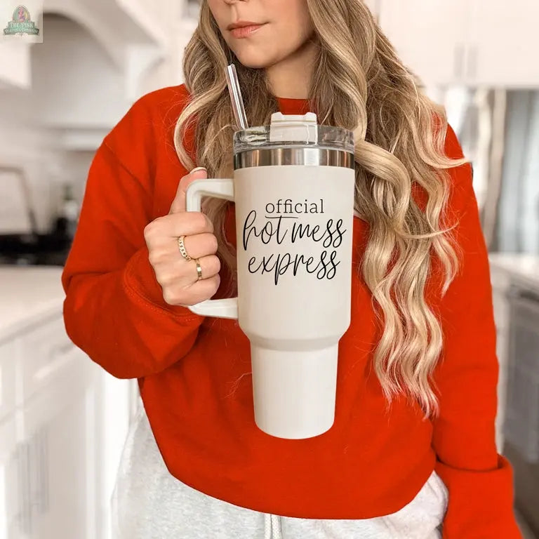 A woman in a red sweatshirt stands in a bright kitchen, holding the Official Hot Mess 40oz tumbler with straw, adding a playful vibe to her morning routine.